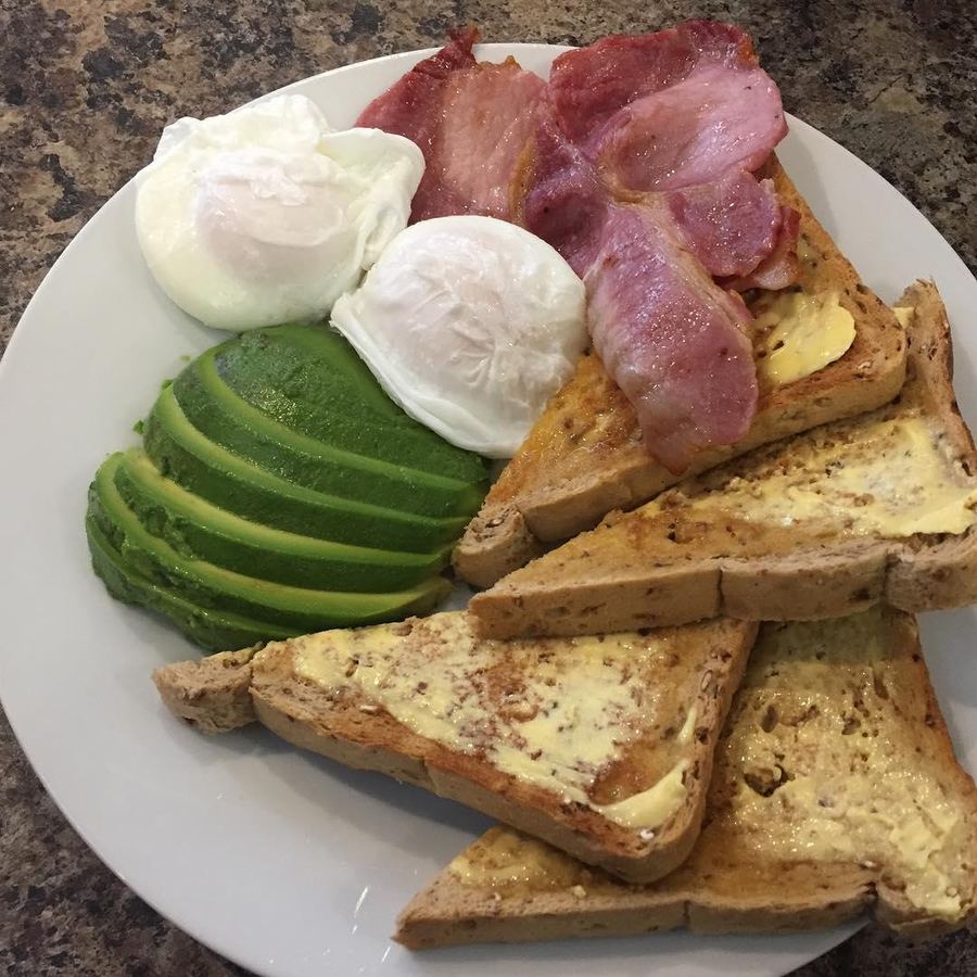 Poached eggs, bacon, sliced avocado and buttered granary toast on a white plate