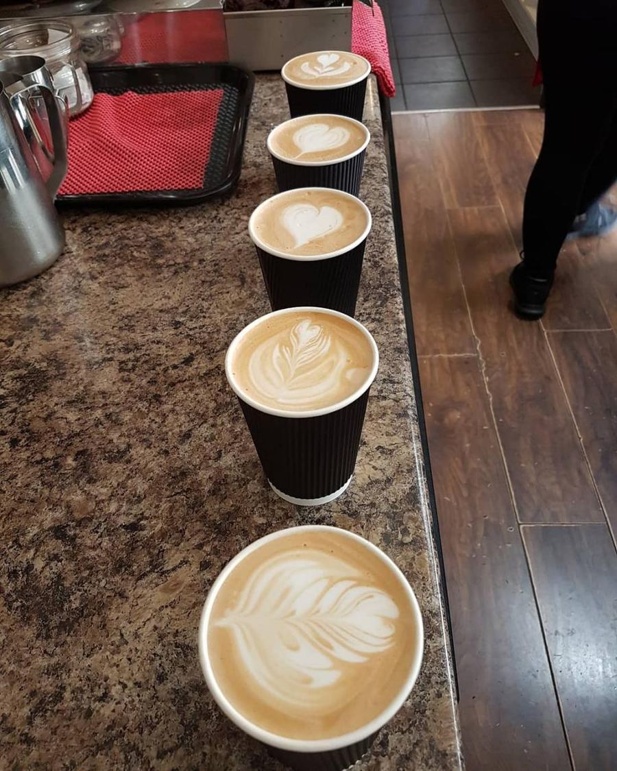 A row of five takeaway coffees, each poured with latte art