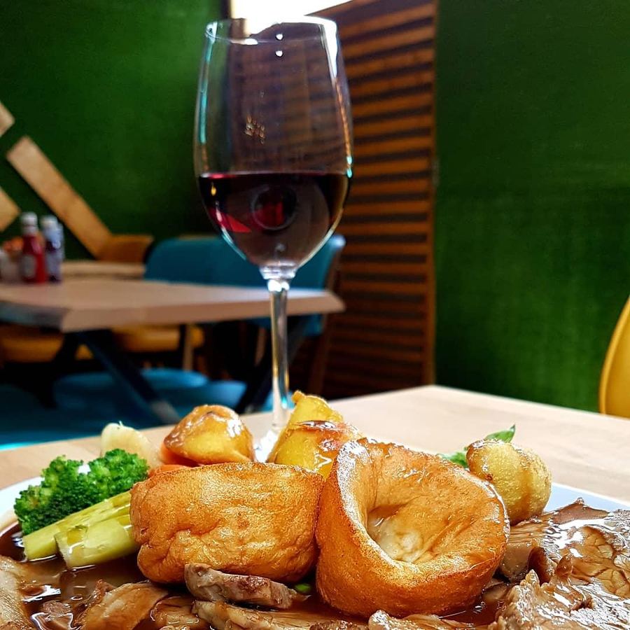 A roast dinner with Yorkshire puddings and gravy, a glass of red wine behind it