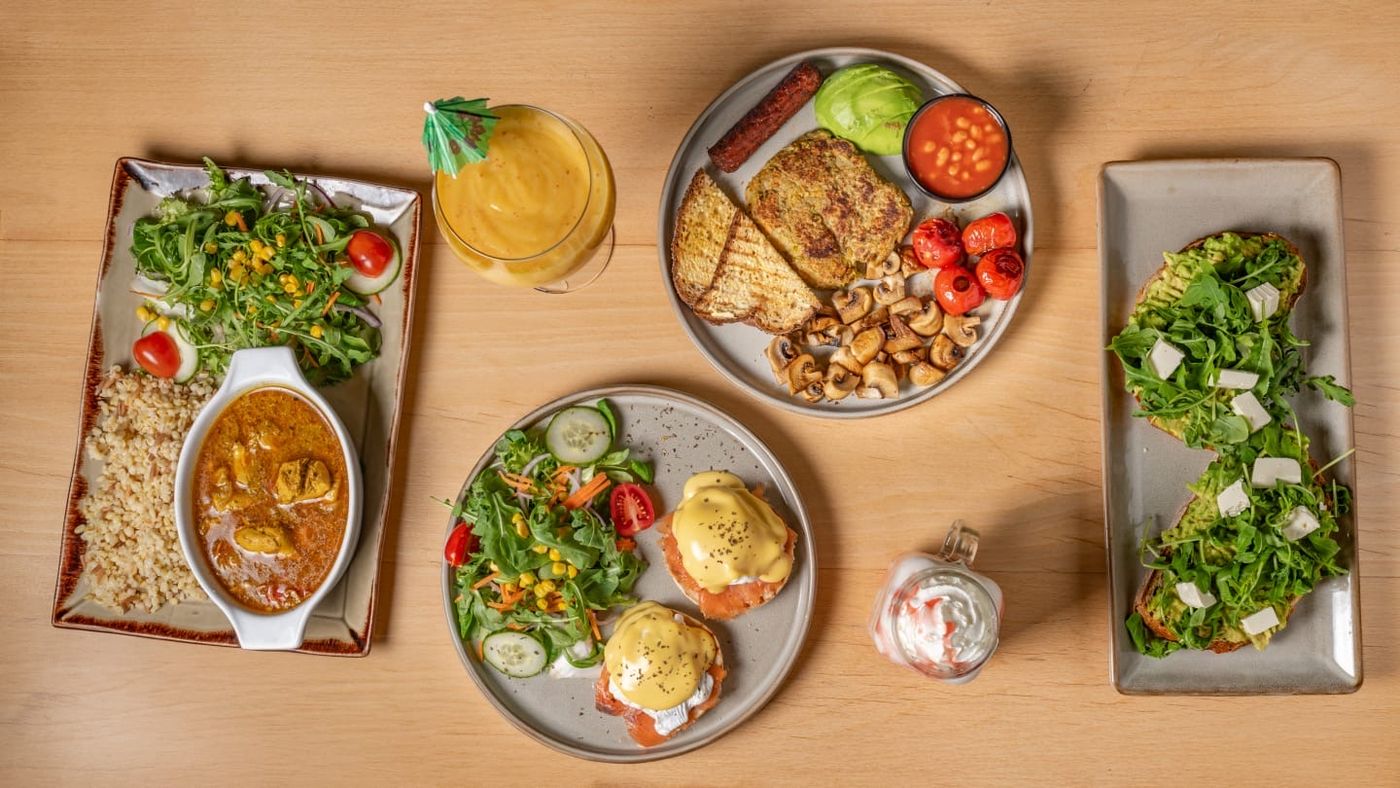 An On A Plate table from above: chicken curry with rice, eggs royale, cooked breakfast, avocado on toast and a mango smoothie